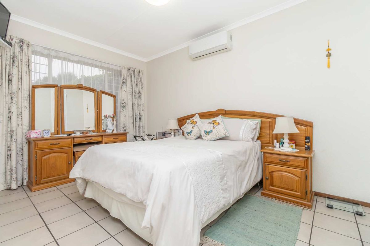 A well-lit bedroom featuring tiled flooring, coving, and a wall-mounted split-system air conditioning unit.