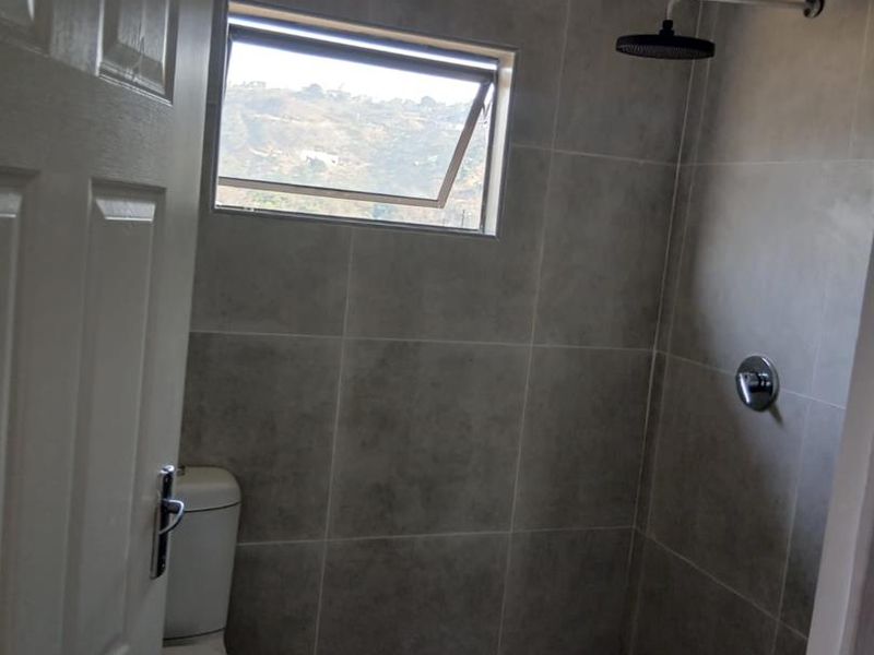 A modern bathroom featuring grey wall tiles, a patterned tiled shower floor, a wall-mounted shower head, and a toilet.