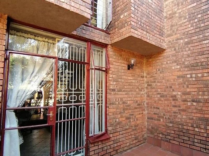 A private rear patio area featuring face brick walls, tiled flooring, and secure metal-framed glass doors leading into the home.