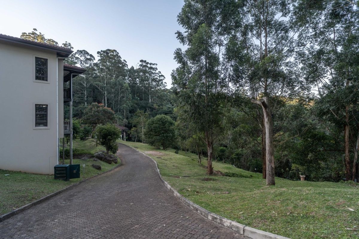 A view of the rear exterior of the townhouse, featuring a paved driveway leading through a well-maintained garden with mature trees.