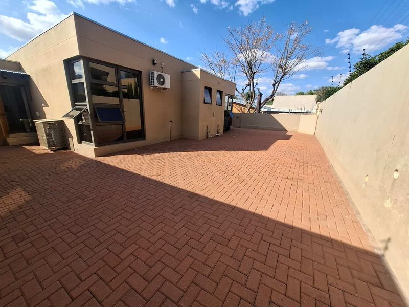 A spacious, low-maintenance paved rear courtyard featuring a boundary wall and exterior air conditioning unit, ideal for outdoor living.