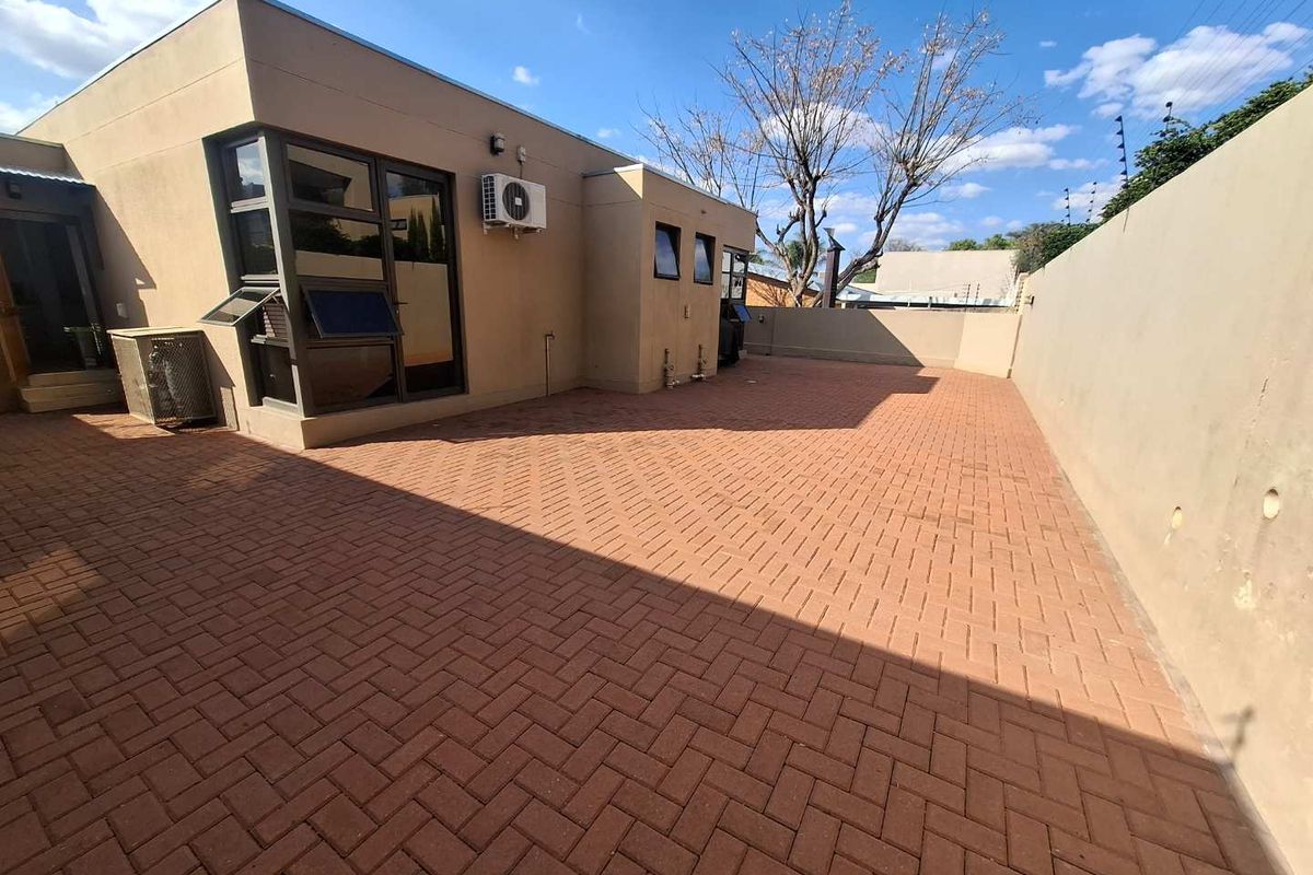 A spacious, low-maintenance paved rear courtyard featuring a boundary wall and exterior air conditioning unit, ideal for outdoor living.