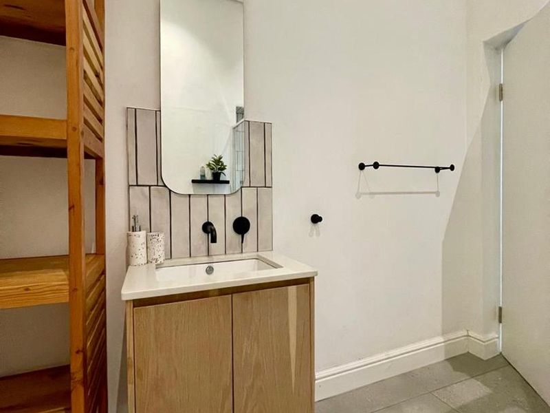 A modern bathroom featuring a vanity cabinet with a basin, tiled splashback, and wall-mounted mirror, finished with neutral floor tiles.