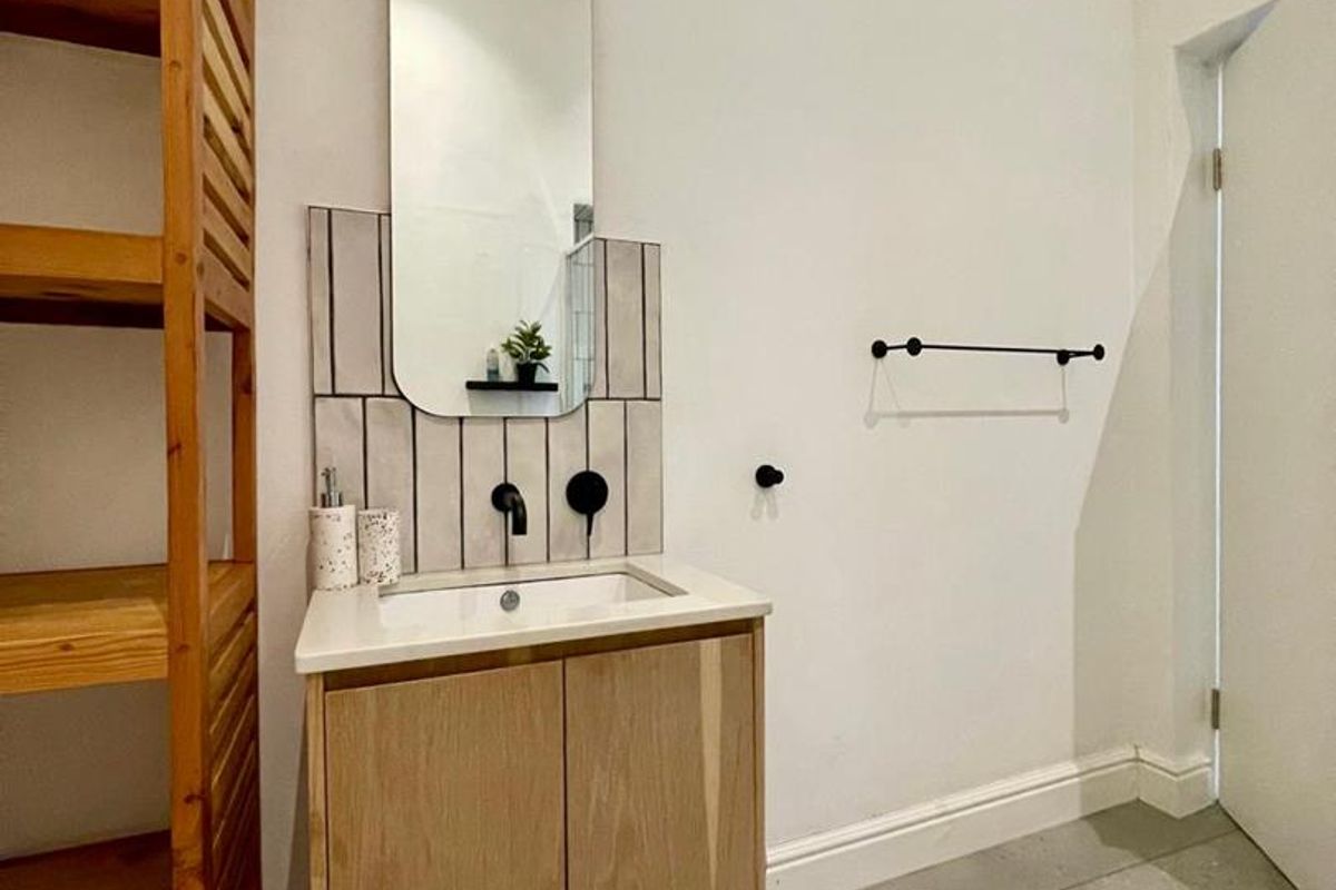 A modern bathroom featuring a vanity cabinet with a basin, tiled splashback, and wall-mounted mirror, finished with neutral floor tiles.