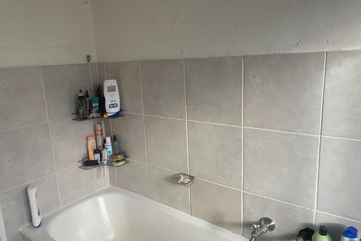 A bathroom area featuring a standard bathtub with wall-mounted taps and tiled splashback surrounds.