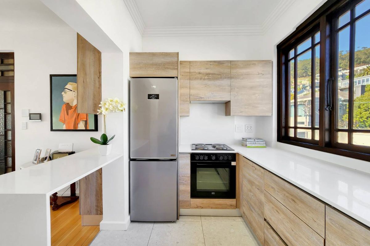 Modern kitchen featuring wood-grain cabinetry, stone countertops, built-in oven and hob, and a breakfast bar area with clean, contemporary finishes.