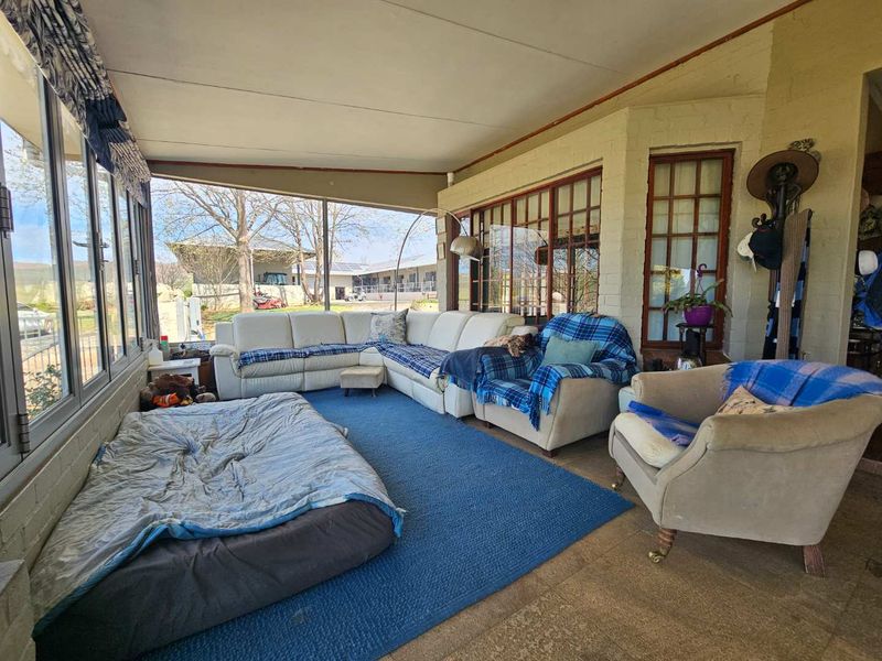 A spacious covered patio area featuring large glass sliding doors, tiled flooring, and painted brick walls, offering a comfortable outdoor living space.