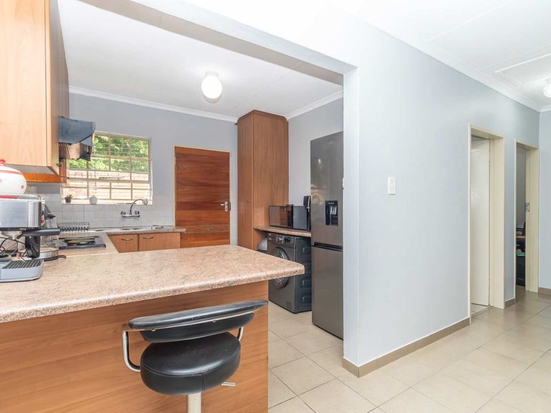 Open plan kitchen featuring laminate cabinetry, tiled flooring, and a breakfast bar, seamlessly connecting to the adjacent hallway and living area.