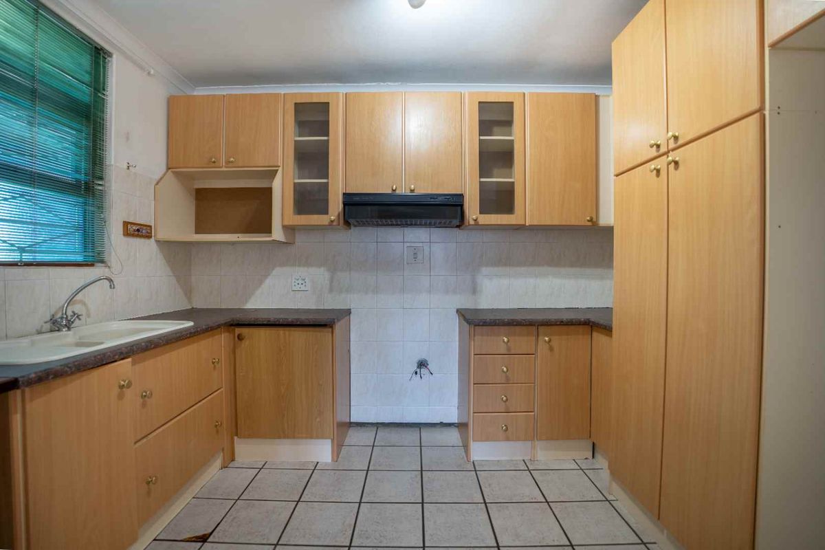 A dated kitchen featuring light wood cabinetry, laminate countertops, and tiled flooring. The space is currently vacant and requires a new stove or hob.