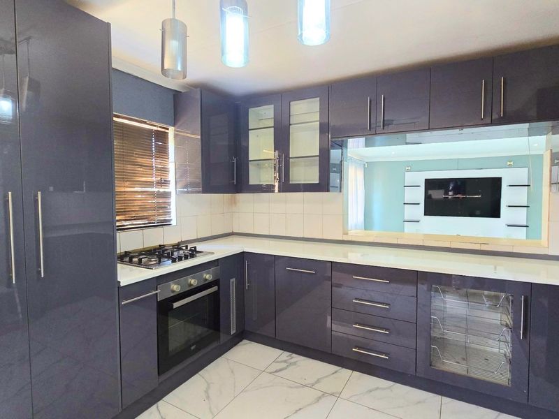 Modern kitchen featuring high-gloss cabinetry, stone countertops, built-in oven, gas hob, and elegant tiled flooring with contemporary pendant lighting.