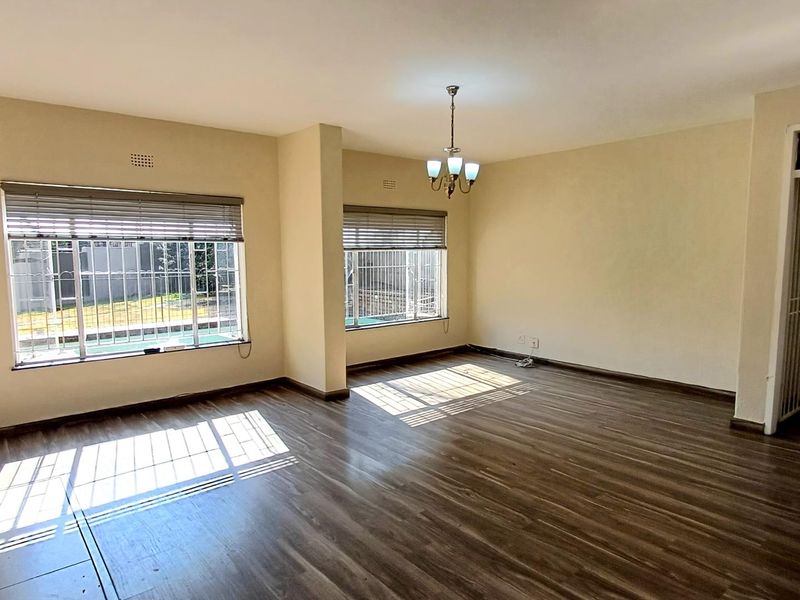 Spacious, sunlit living area featuring modern laminate flooring, security bars on windows, and neutral wall finishes, offering a versatile blank canvas.