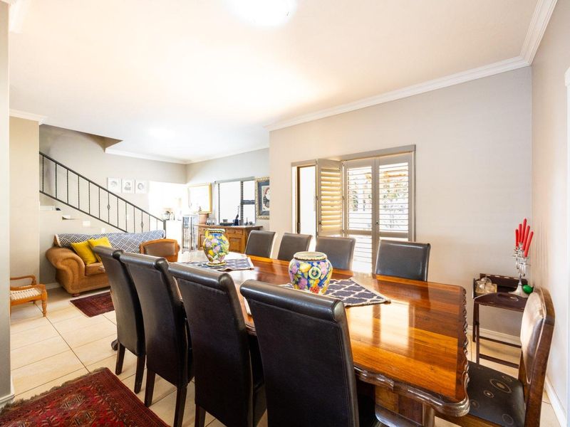 Spacious dining area featuring tiled flooring, crown molding, and plantation shutters, with an open-plan layout leading to a staircase with a wrought iron balustrade.