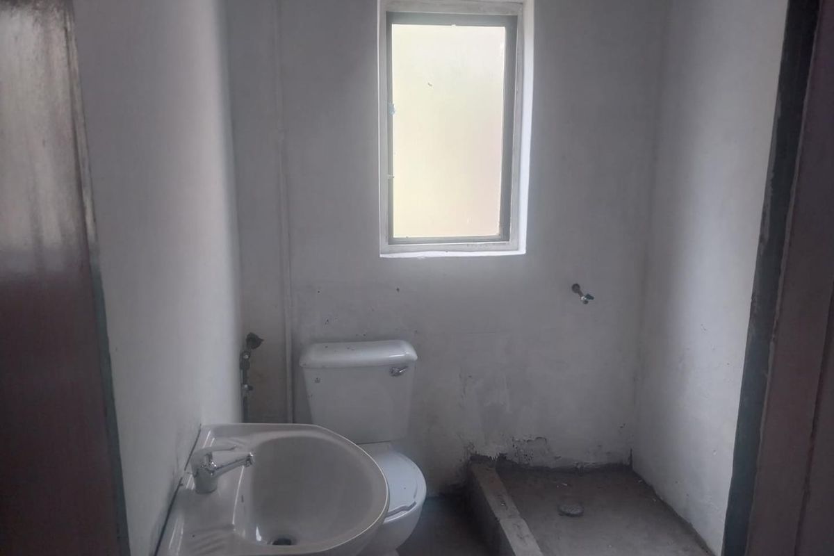 A small, unfinished bathroom featuring a basic toilet and pedestal basin, requiring flooring and wall finishing to complete the space.