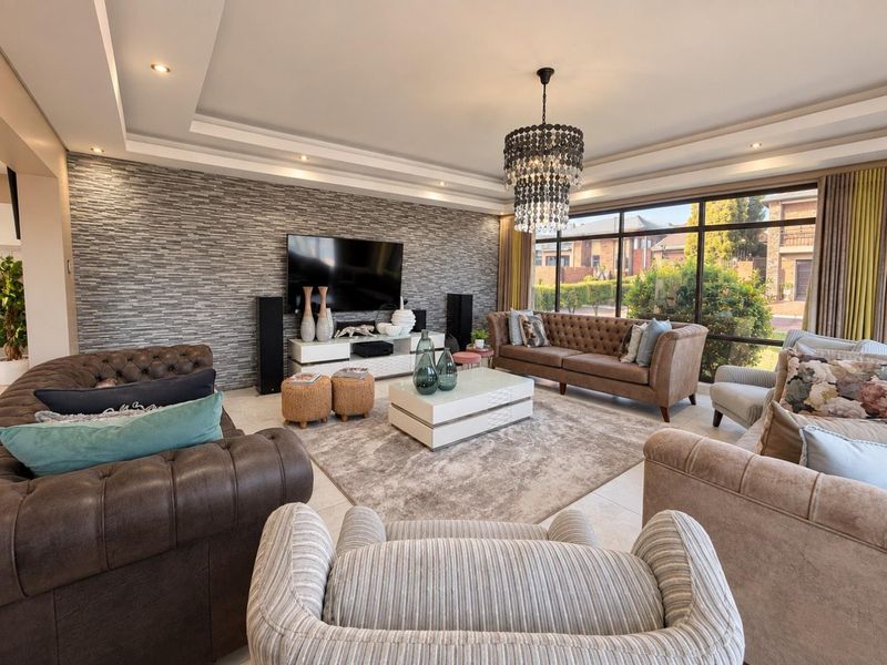 Spacious living room featuring a modern stone feature wall, recessed ceiling with downlights, elegant chandelier, and large windows providing ample natural light.