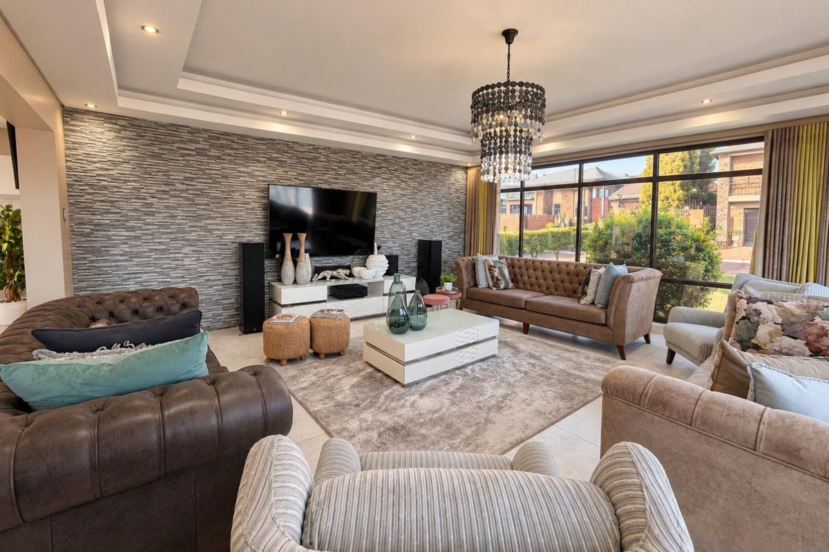 Spacious living room featuring a modern stone feature wall, recessed ceiling with downlights, elegant chandelier, and large windows providing ample natural light.