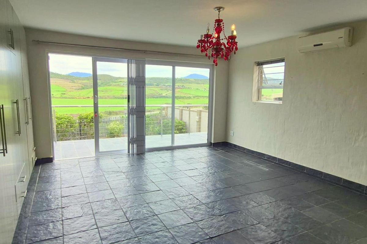 Spacious bedroom featuring dark slate flooring, built-in cabinetry, wall-mounted air conditioning unit, and sliding glass doors opening to a scenic balcony view.