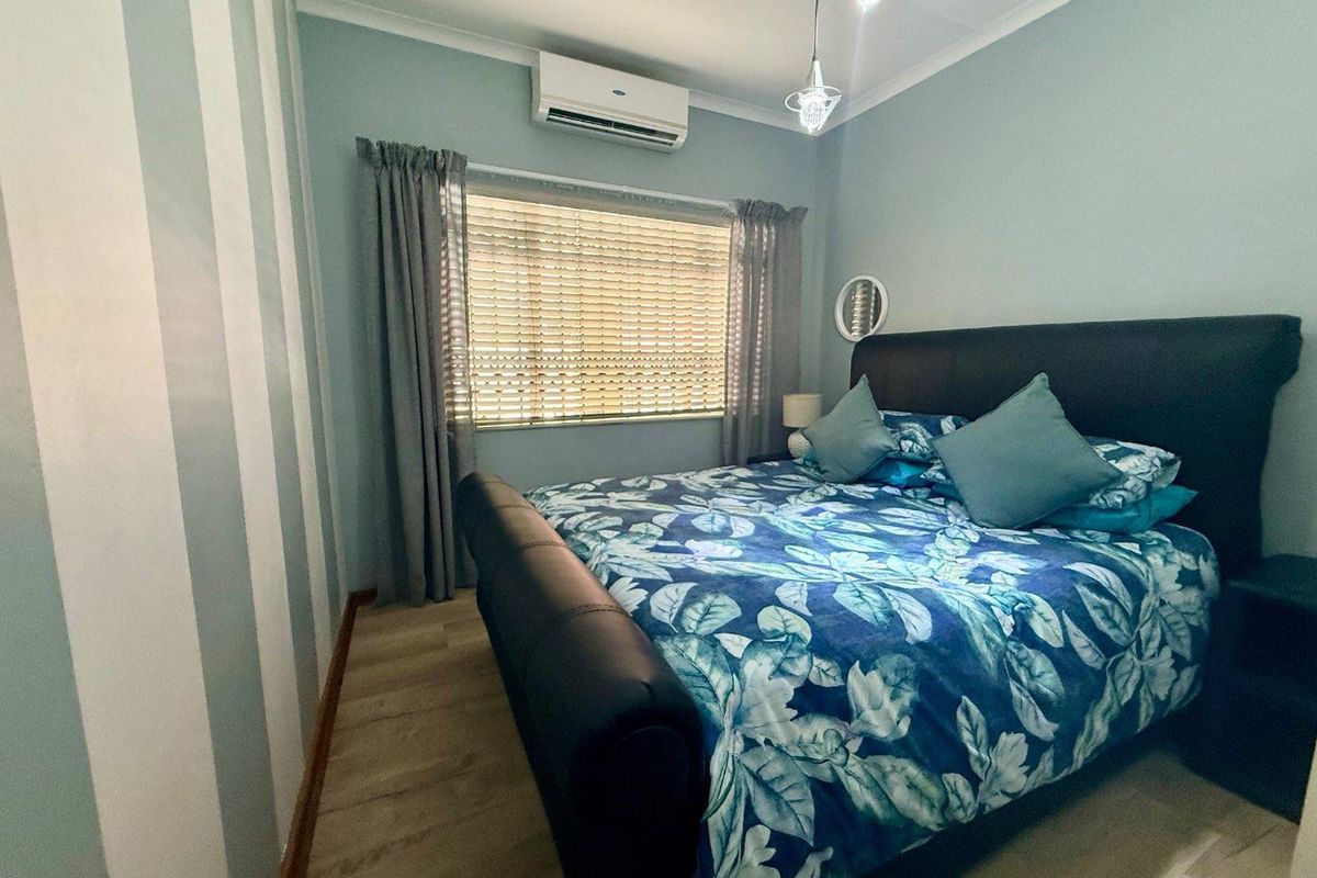 A well-maintained bedroom featuring light-toned laminate flooring, a wall-mounted air conditioning unit, and decorative striped wall accents.