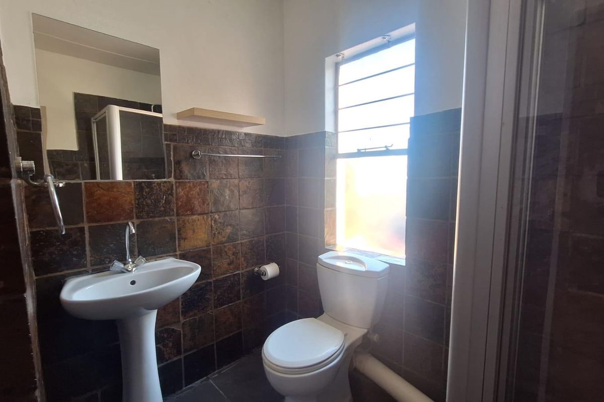 A functional bathroom featuring a pedestal basin, toilet, and shower enclosure with dark slate-style wall tiling and a window for natural light.