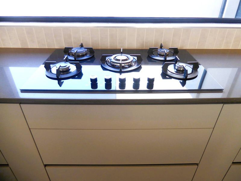 A modern kitchen featuring a sleek built-in gas cooktop set into a stone countertop with minimalist handleless cabinetry.