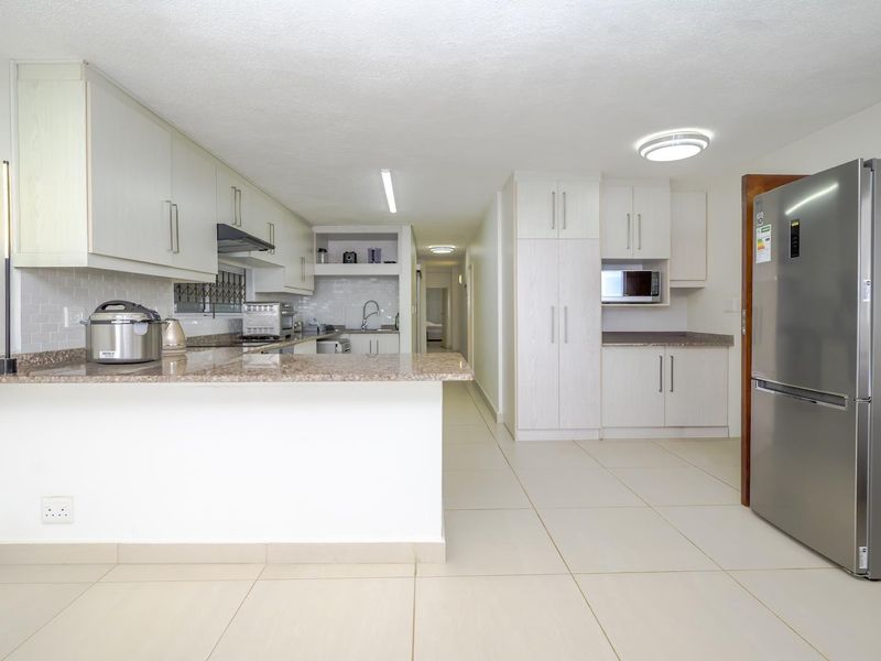 A well-maintained kitchen featuring light-toned cabinetry, granite countertops, a subway tile backsplash, and integrated appliances, flowing into an open-plan living area.