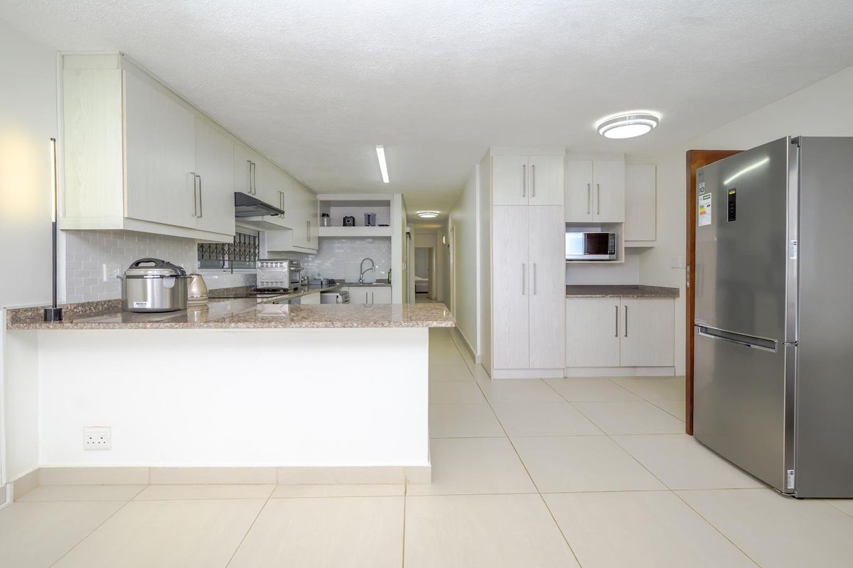 A well-maintained kitchen featuring light-toned cabinetry, granite countertops, a subway tile backsplash, and integrated appliances, flowing into an open-plan living area.