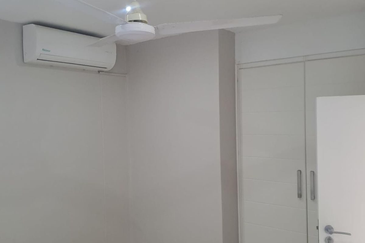 A clean, neutral-toned bedroom featuring a built-in wardrobe, ceiling fan, and wall-mounted air conditioning unit.