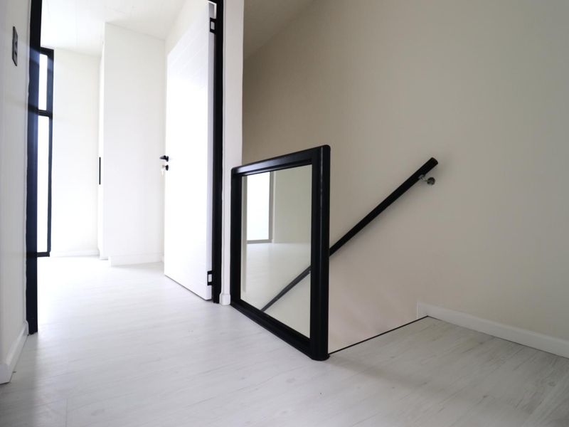A bright, modern hallway featuring a staircase with a sleek black-framed glass balustrade and minimalist interior doors.
