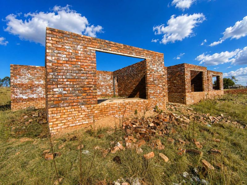 An unfinished brick structure showing the exterior shell of a building under construction on a rural property.