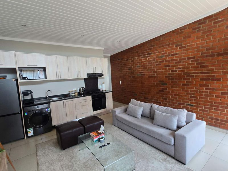 Modern open-plan living area featuring a functional kitchen with built-in cabinetry, integrated appliances, and a striking exposed brick feature wall.