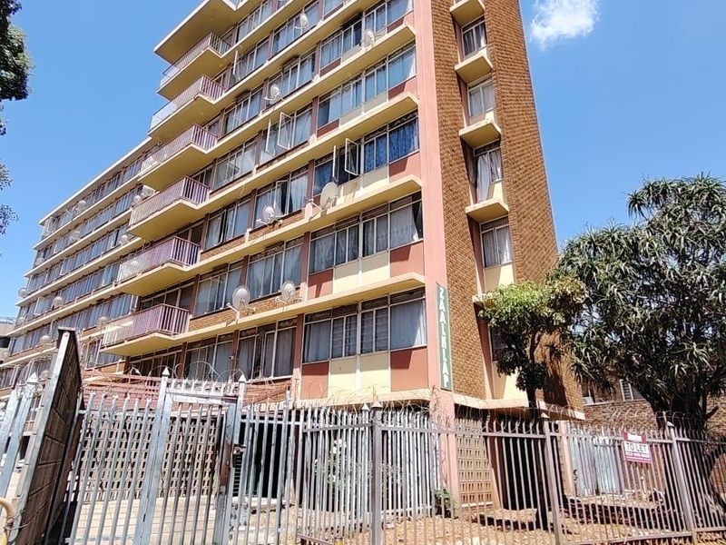 Exterior view of a multi-story apartment building featuring balconies, security fencing, and a gated entrance.