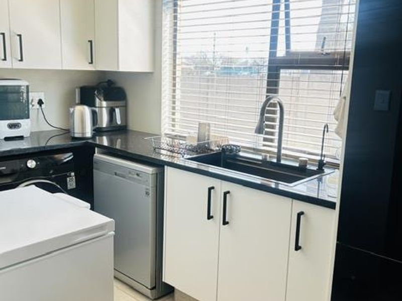 Modern kitchen featuring white cabinetry, dark granite countertops, an undermount sink with a gooseneck faucet, and tiled flooring.