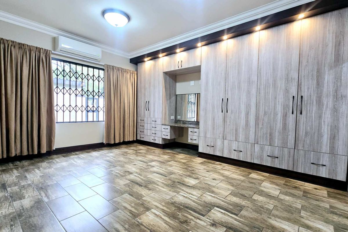 Spacious bedroom featuring extensive built-in cabinetry with an integrated vanity, tiled flooring, and a wall-mounted air conditioning unit.