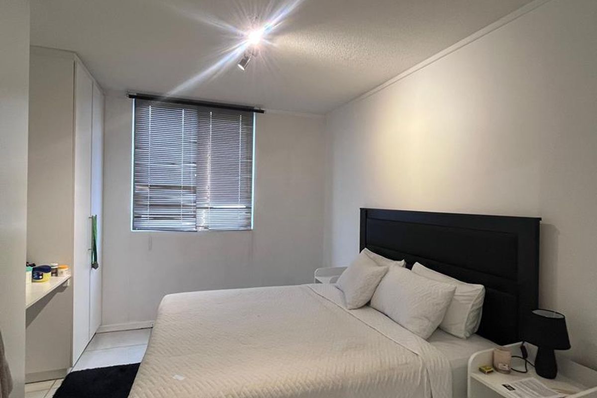 A bright bedroom featuring built-in cupboards, tiled flooring, and a window fitted with horizontal blinds.