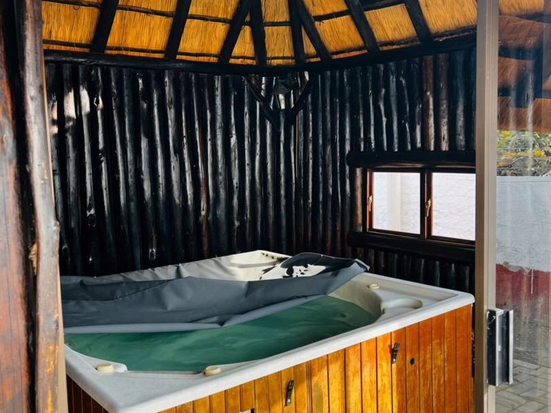 A rustic indoor hot tub area featuring a thatched roof, timber log walls, and a built-in spa unit.