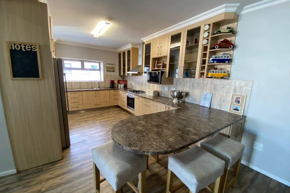 A well-maintained kitchen featuring light wood cabinetry, stone-look countertops, a breakfast bar, and integrated appliances including a built-in oven and extractor fan.