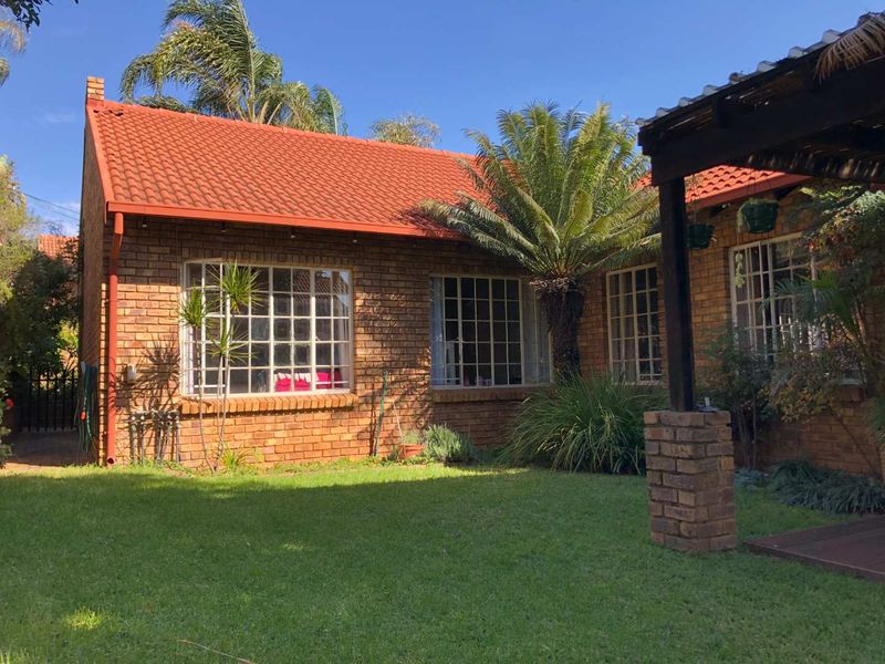 Rear view of a face brick house featuring a tiled roof, steel frame windows, and a timber pergola overlooking a well-maintained garden.