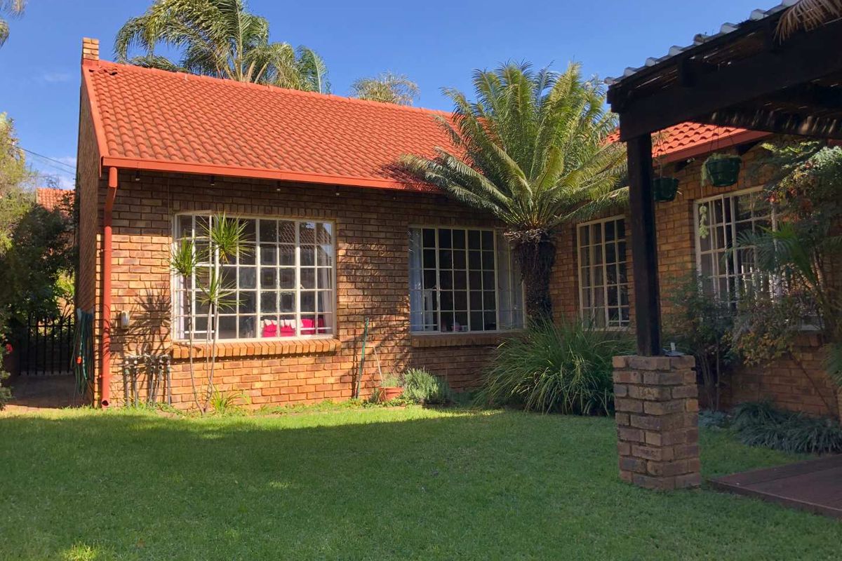 Rear view of a face brick house featuring a tiled roof, steel frame windows, and a timber pergola overlooking a well-maintained garden.