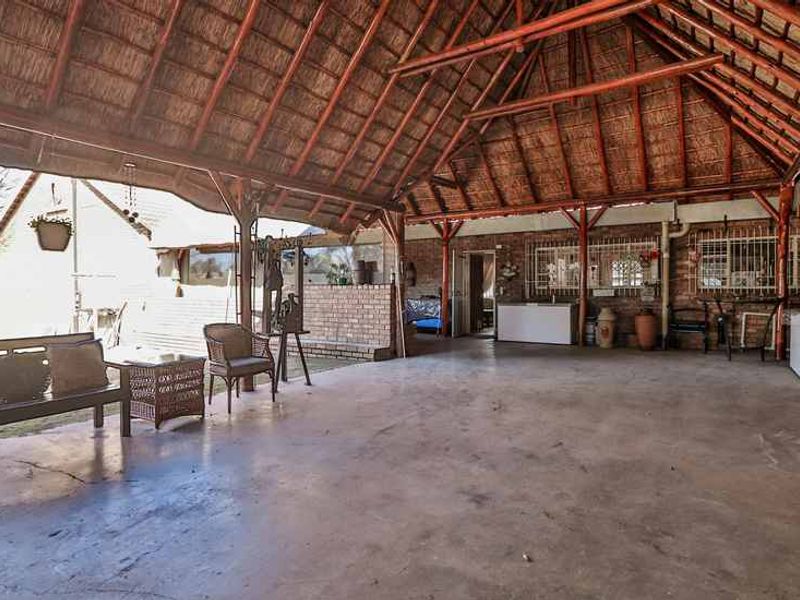 Spacious covered patio featuring a traditional thatched roof with exposed timber trusses and durable concrete flooring, ideal for outdoor entertaining.