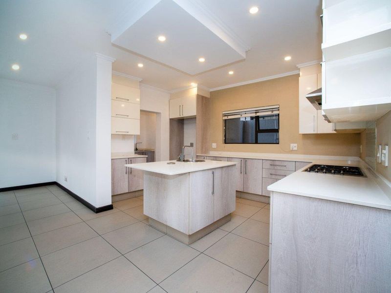 Modern kitchen featuring a central island, built-in cabinetry, gas cooktop, extractor fan, and tiled flooring, offering a clean and functional workspace.