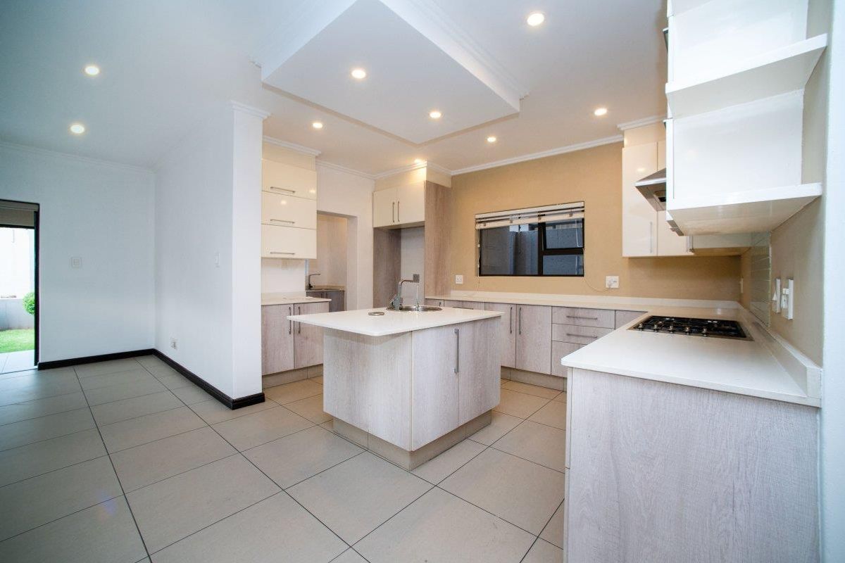 Modern kitchen featuring a central island, built-in cabinetry, gas cooktop, extractor fan, and tiled flooring, offering a clean and functional workspace.