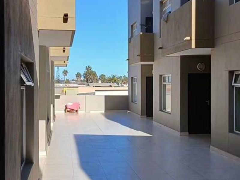A spacious, tiled outdoor balcony area connecting apartment units, featuring clean lines and modern exterior finishes.
