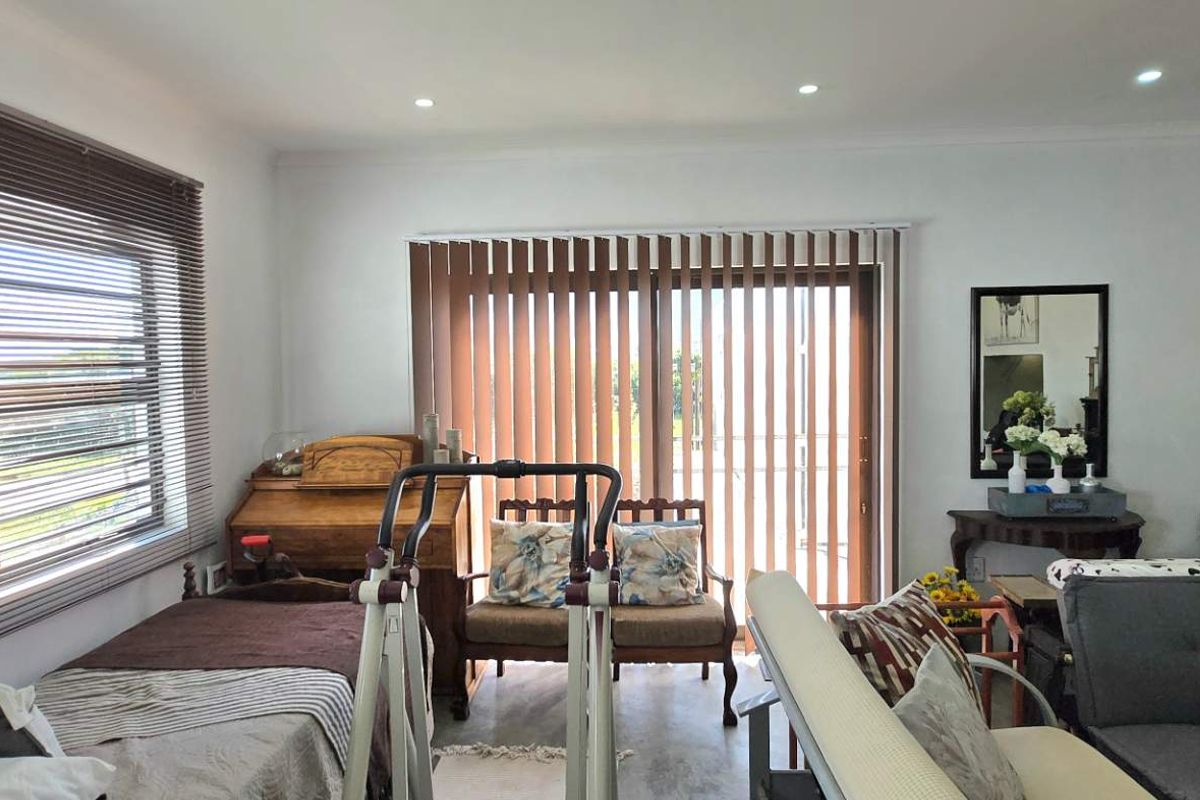 A bright living area featuring large windows with fitted blinds, recessed ceiling lighting, and sliding glass doors leading to an outdoor space.
