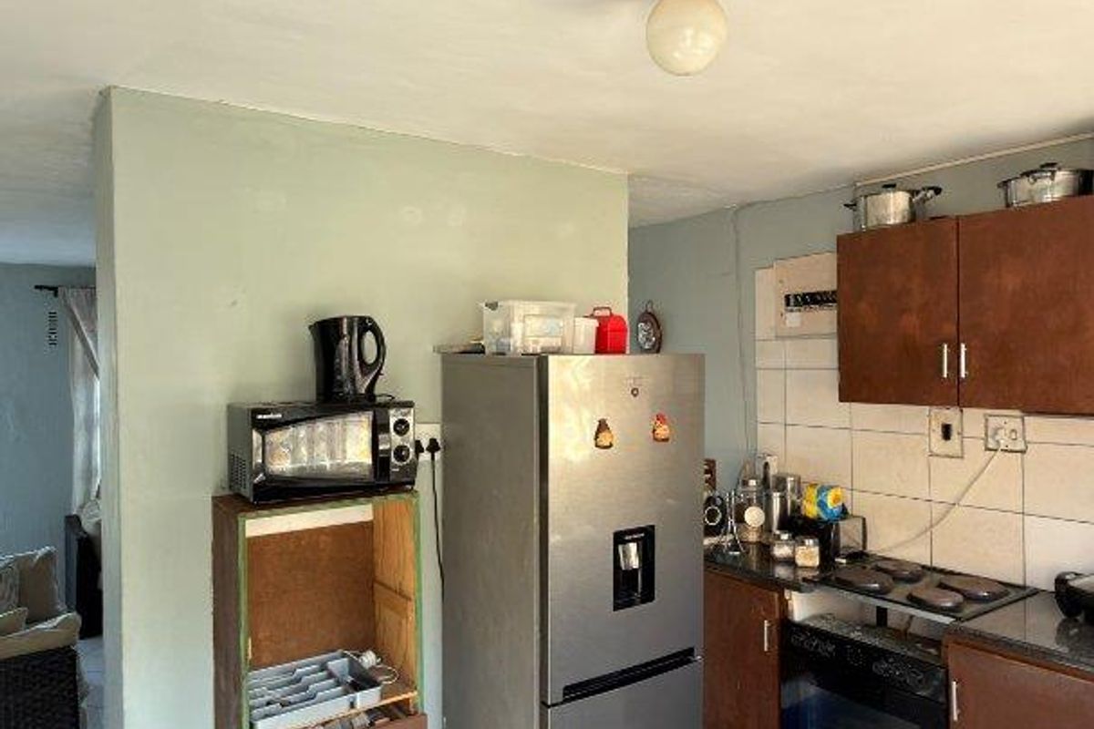 A functional kitchen featuring built-in cabinetry, an oven, and hob, with tiled flooring and backsplash, offering potential for modernization and cosmetic updates.