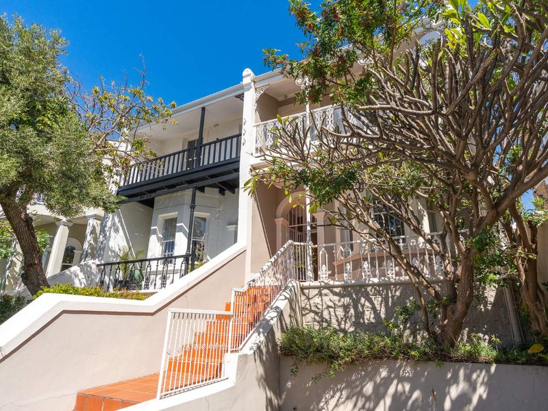 Charming multi-level Victorian-style townhouse facade featuring a classic wrought iron balcony, tiled entrance staircase, and established garden setting.