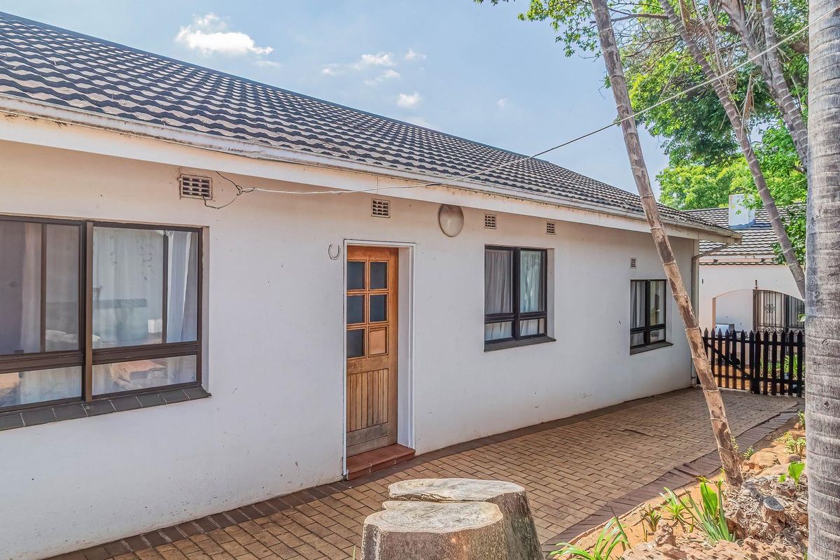 Rear exterior view of the house featuring a paved walkway, tiled roof, and timber entrance door with aluminium window frames.