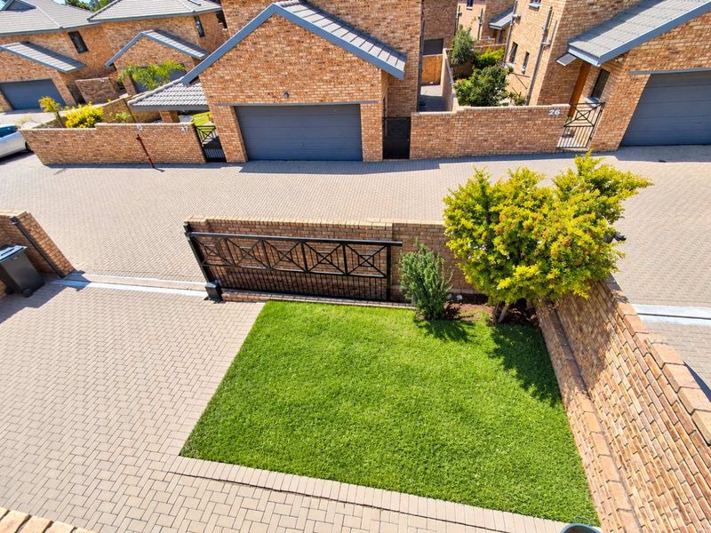Aerial view of a townhouse complex featuring face brick facades, paved driveways, private garden areas, and secure metal gate access.