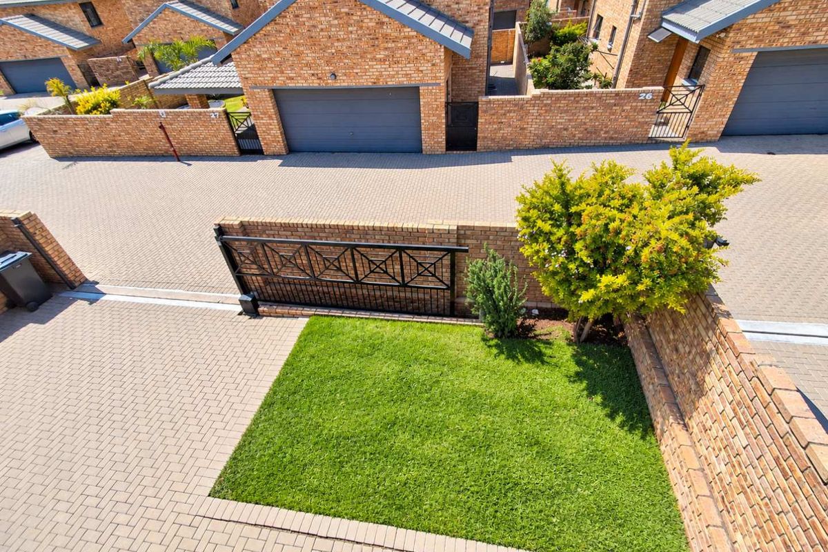 Aerial view of a townhouse complex featuring face brick facades, paved driveways, private garden areas, and secure metal gate access.