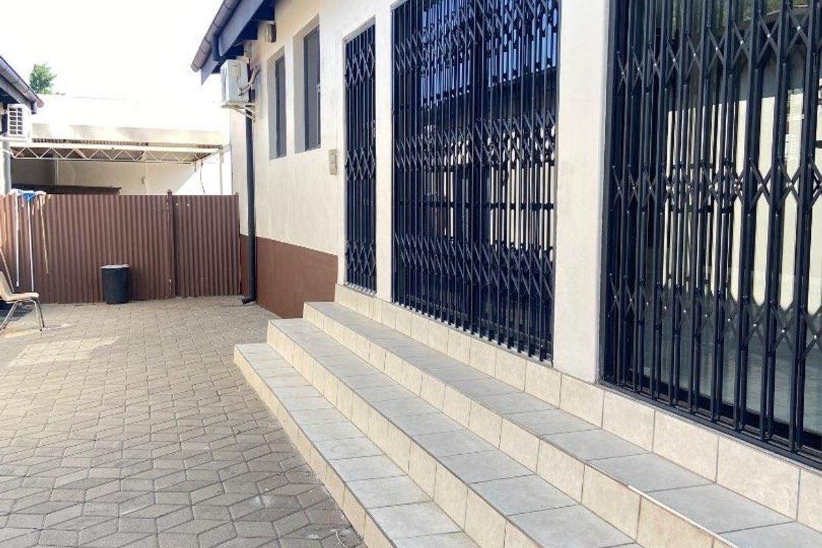 Rear exterior view featuring a paved courtyard, tiled steps leading to the building, and security gates installed on the windows and doors.