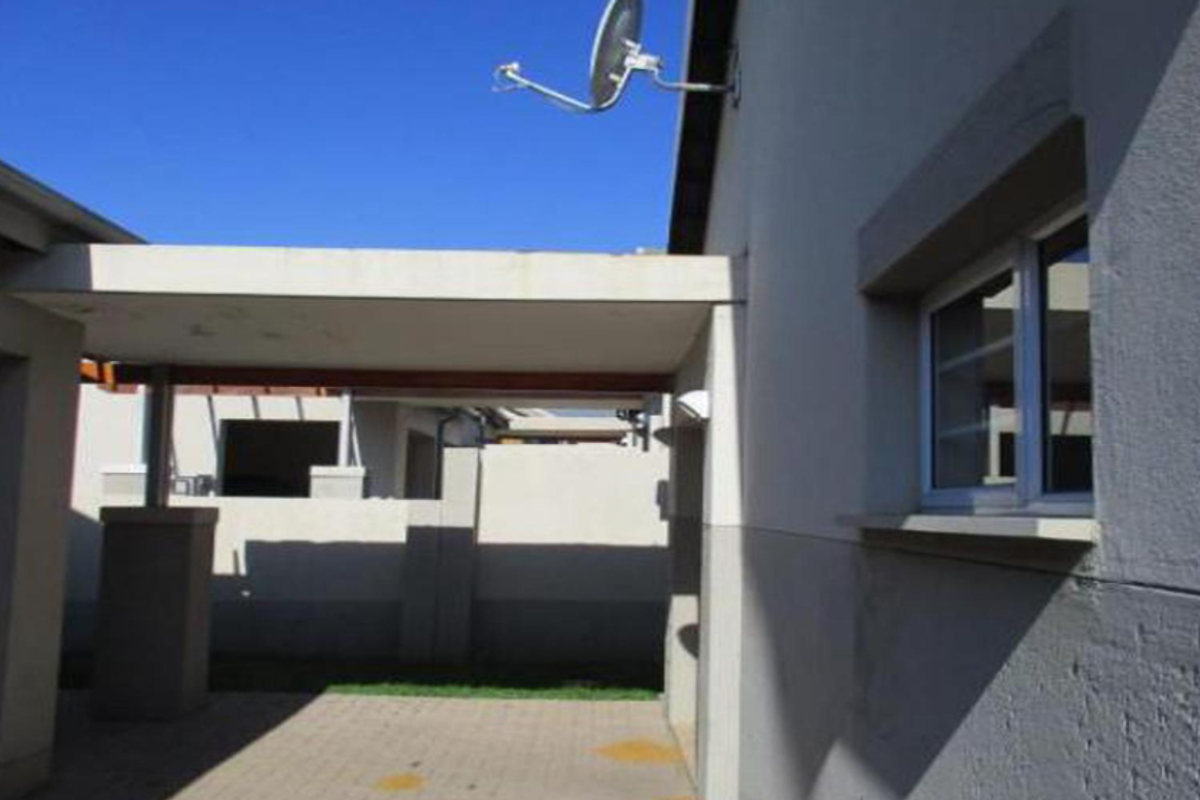 A view of the exterior rear area featuring a covered patio, paved flooring, and a satellite dish mounted on the building facade.