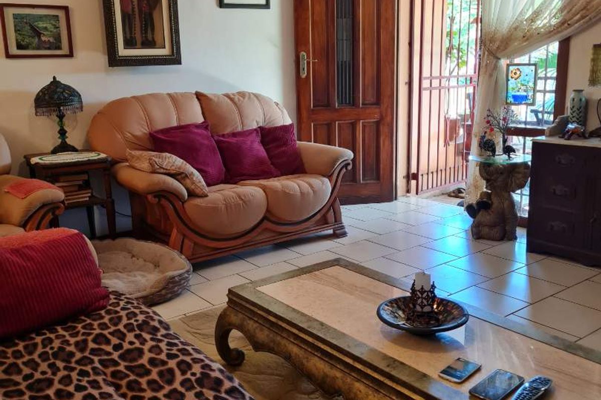 A living room featuring tiled flooring and a solid timber entrance door with security gate access to the exterior.
